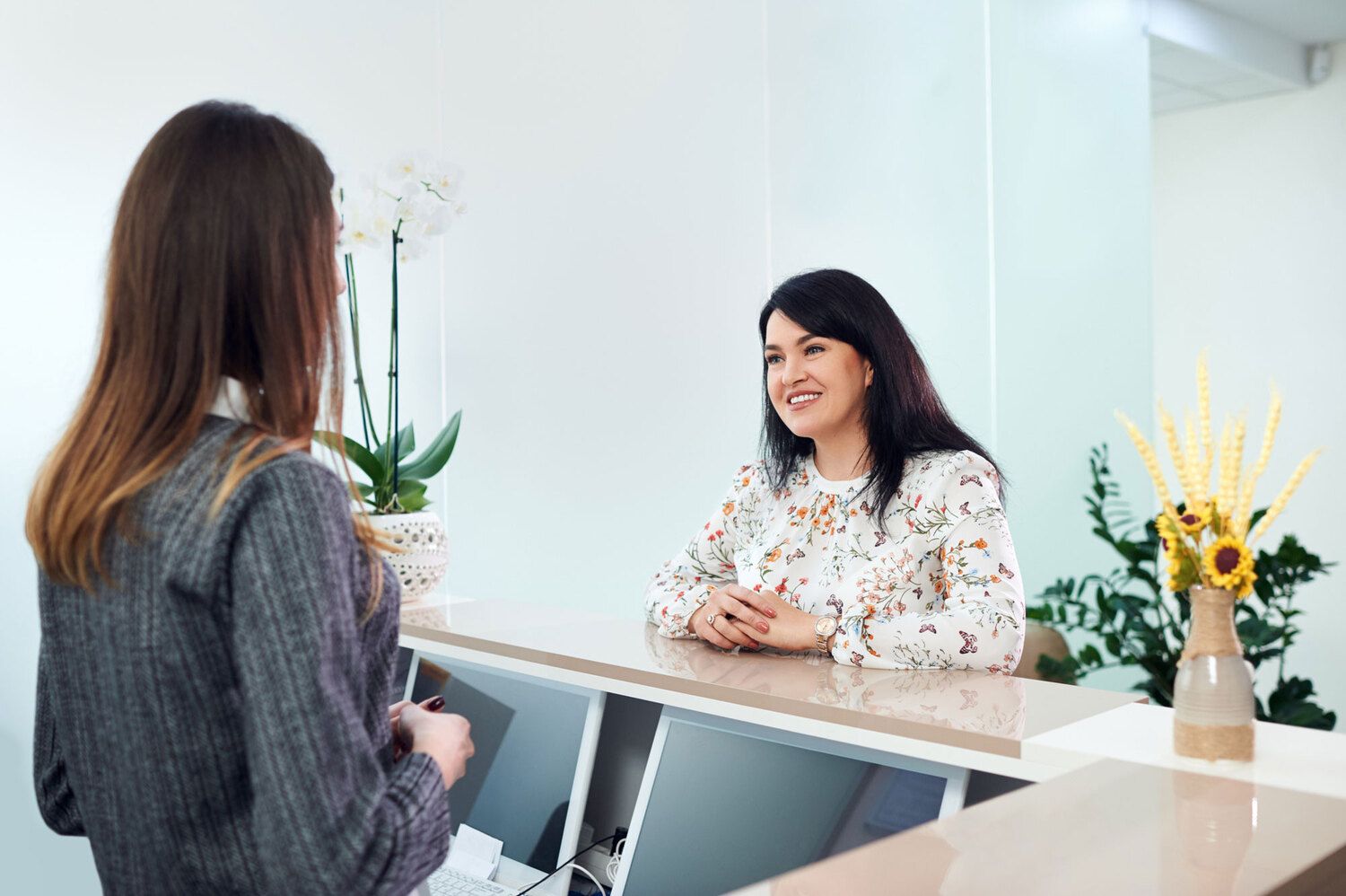Receptionist smiling and assisting a woman at the front desk of a modern dental or medical office.