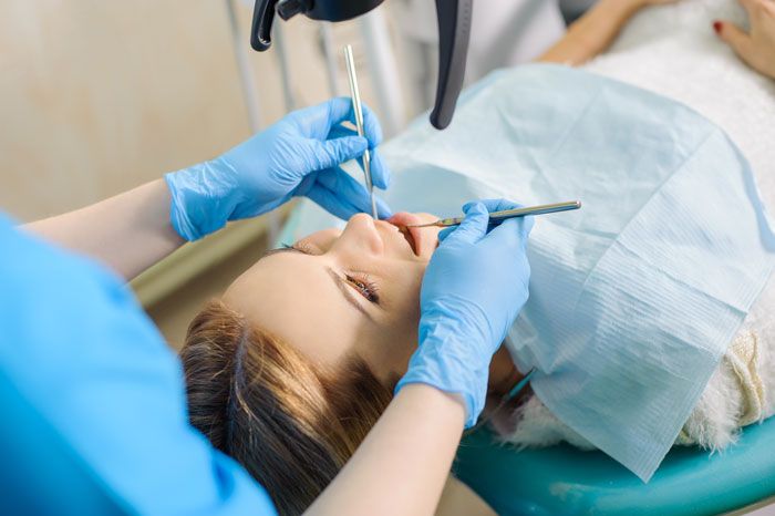 Woman receiving a dental checkup while lying in a dental chair, with dentist's hands using tools.