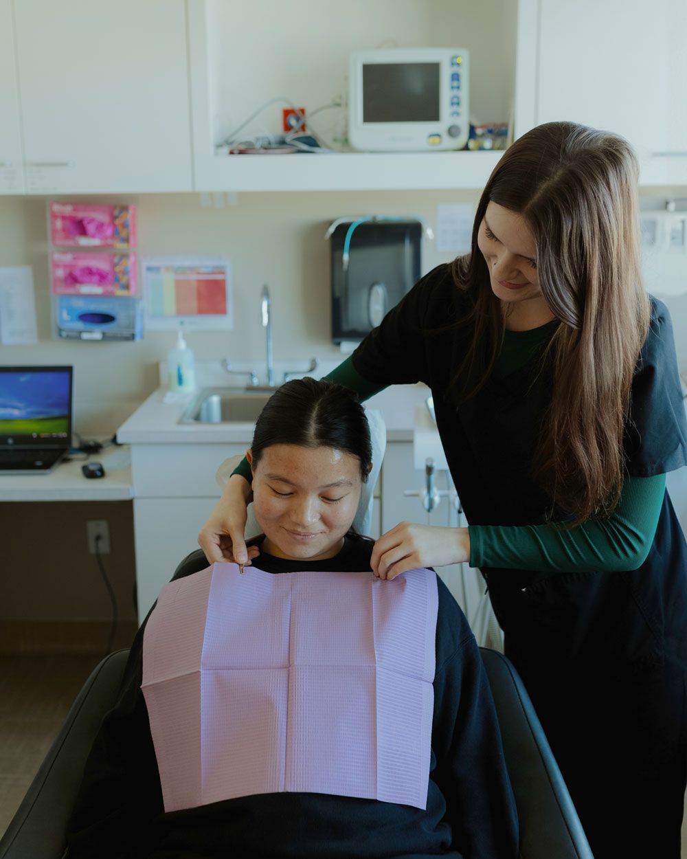 Dental assistant placing a bib on a smiling patient before a dental procedure in a modern clinic.