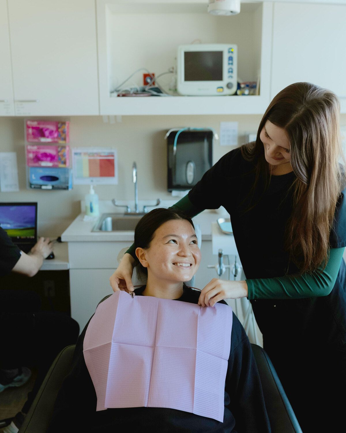 Dental assistant placing a bib on a smiling patient before a dental procedure in a modern clinic.