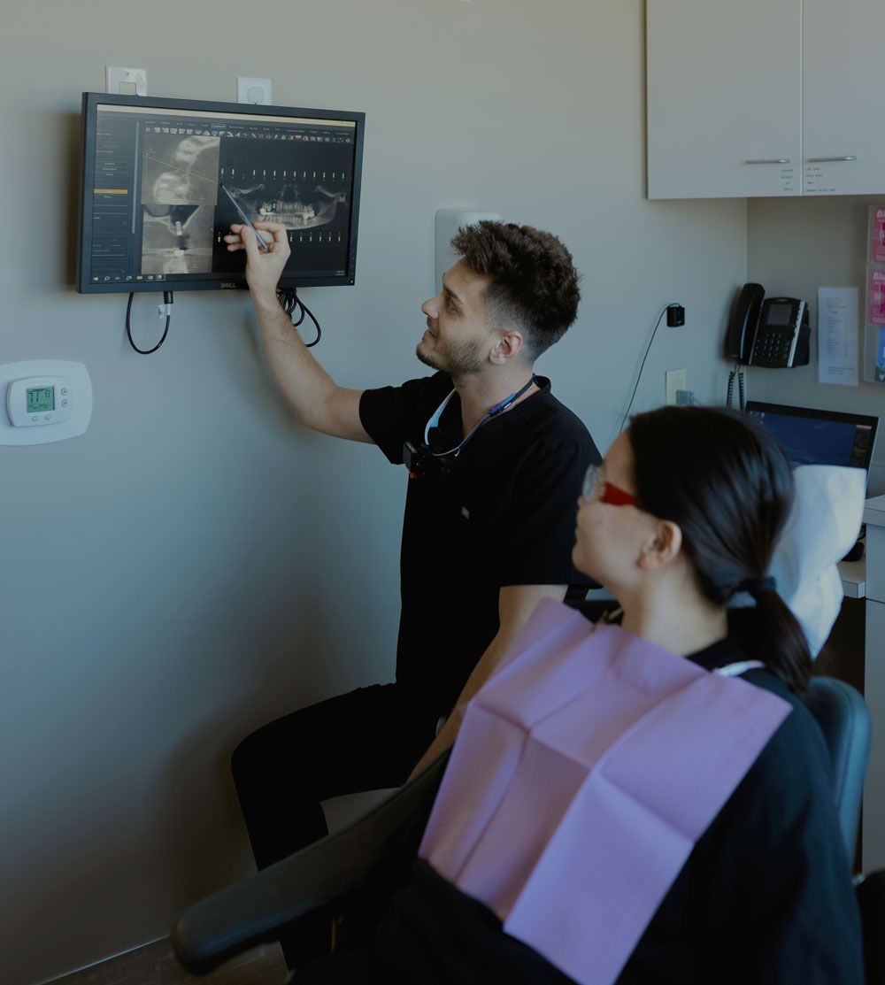 Dentist explaining a dental X-ray to a patient on a wall-mounted screen during a consultation.