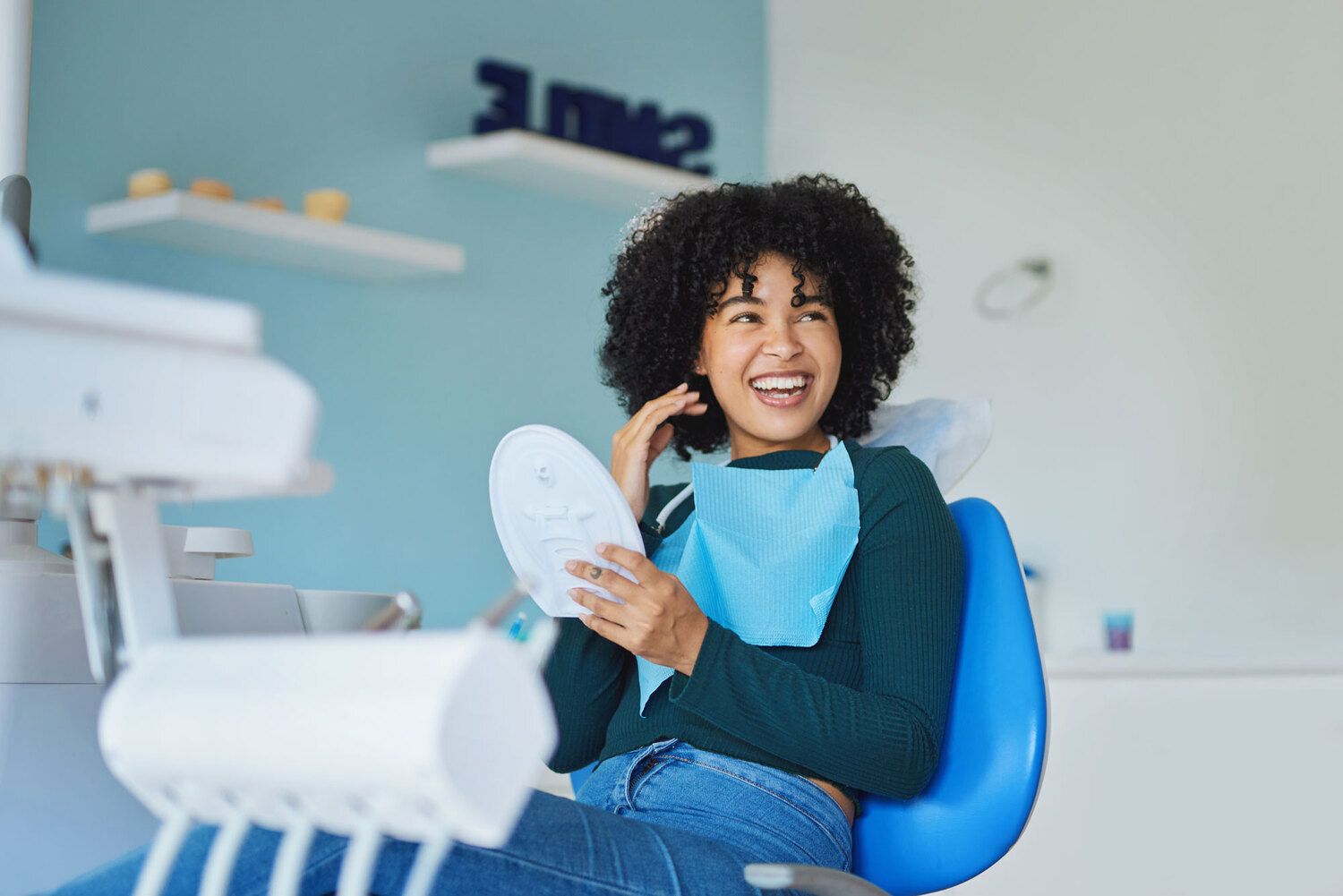 Smiling woman holding a mirror in a dental chair, looking pleased with her results during a dental visit.